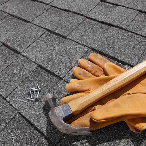 Roofing hammer and gloves resting on new shingles with nails nearby, signifying repair work